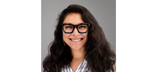 Headshot of smiling woman with long dark hair and thick-rimmed glasses