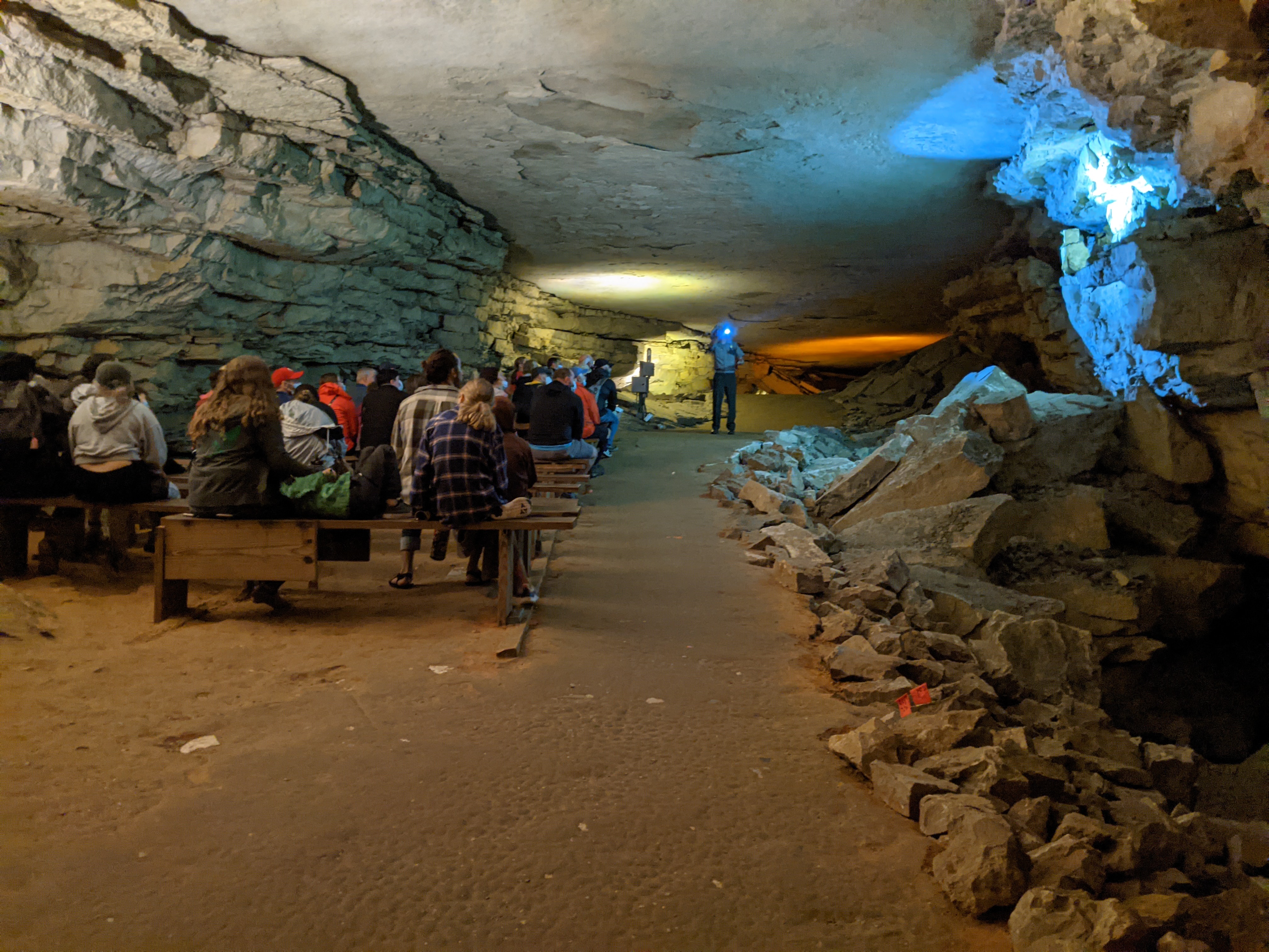 A large cave room with people sitting on wooden benches.