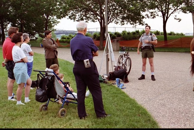 Horton 1 A man wearing shorts stands next to a bike. A tripod is next to him. Several people look on.
