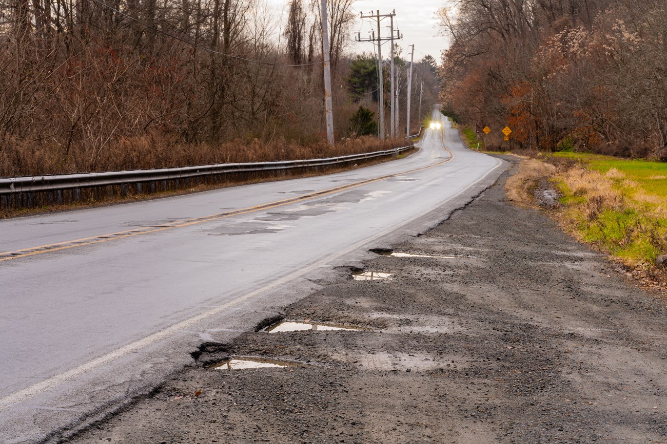 A pot hole scarred U.S. Route 209 with a car coming towards the viewer in the distance