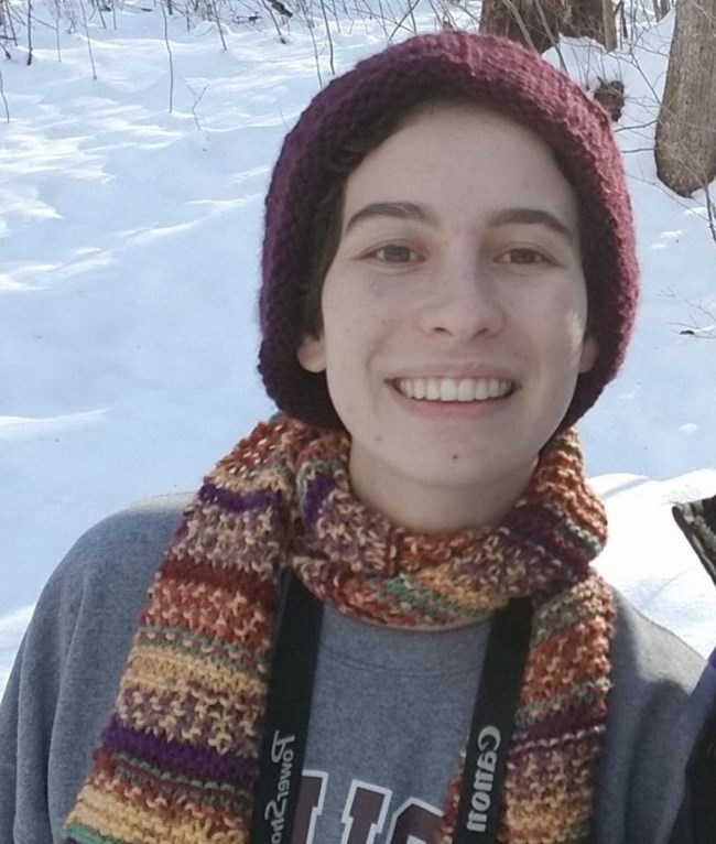 Molly Bahr Woman smiling and wearing winter hat and scarf, with snowy forest scene behind her.