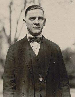 Frank Keeney A man in suit stands in the shade of a nearby tree.