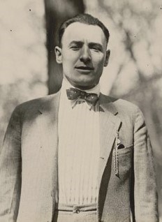 Fred Mooney photo A man in a sit and tie stands in the open air with several trees in the background.