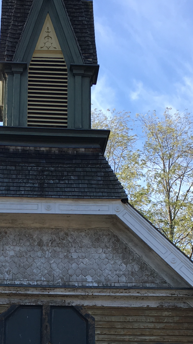 Steeple of the Thompson AME Zion Church in Auburn, NY. A green church steeple with yellow slats and ornamental design in front of the belfry. Weathered shingles top the steeple and the church roof around it.