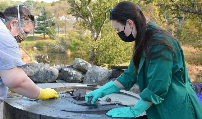 Person wearing gloves and lab coat cleans a bronze landscape model.