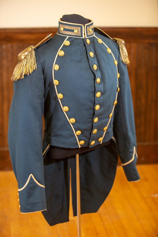 Grey military uniform adorned with golden buttons and golden shoulder pads with frills.