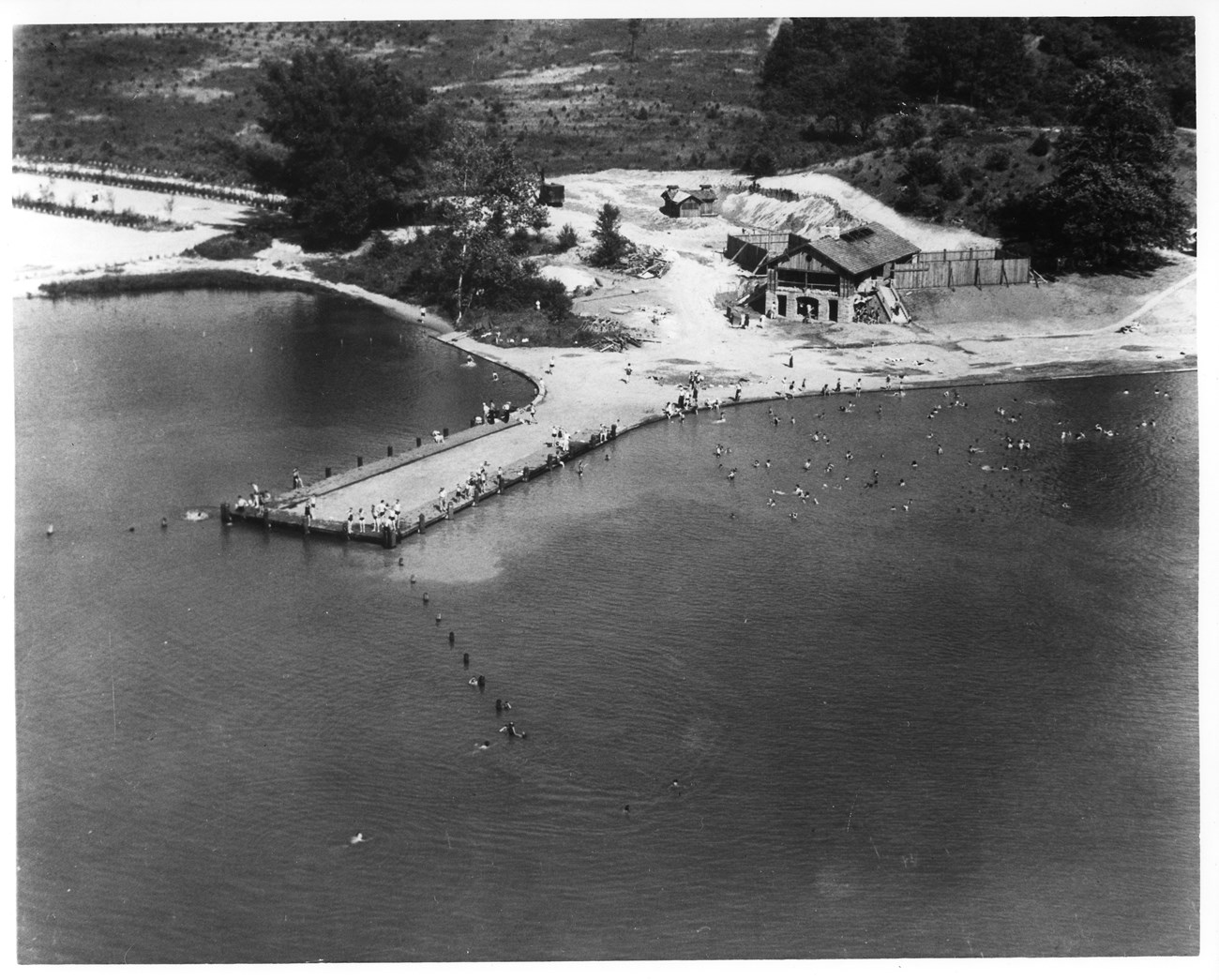 A black-and-white aerial photo of Kendall Lake: a large fishing pier, sandy beach and stone bath house.