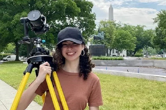 Intern holding a surveying tripod with the Washington Monument in the distance
