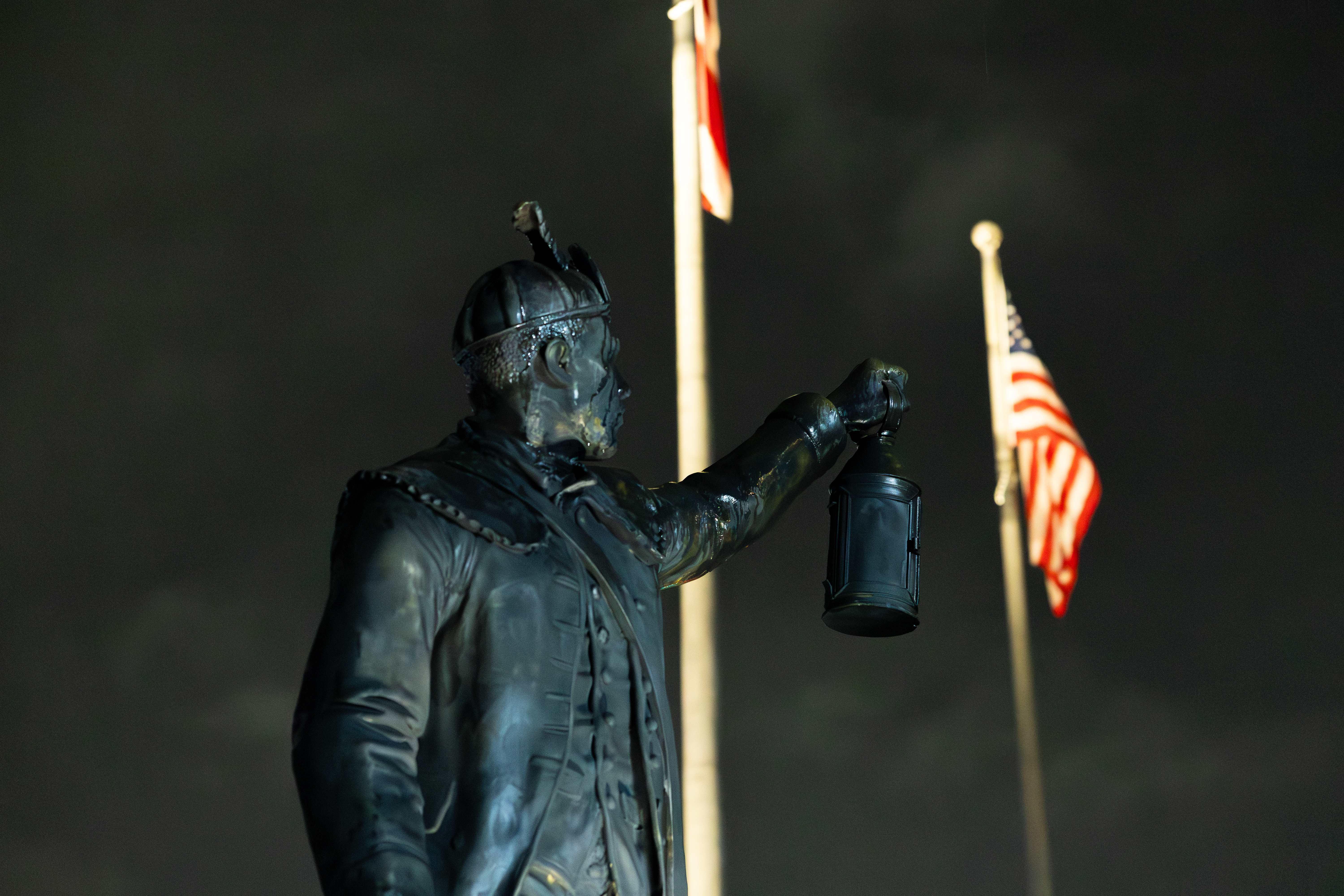 A statue of a man holding up a lantern in front of American flags and a dark sky