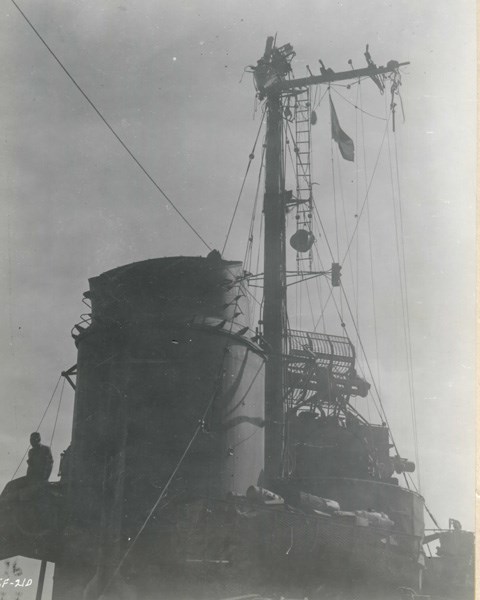 Black and white photograph looking at a mast that is bent with equipment hanging off of it.