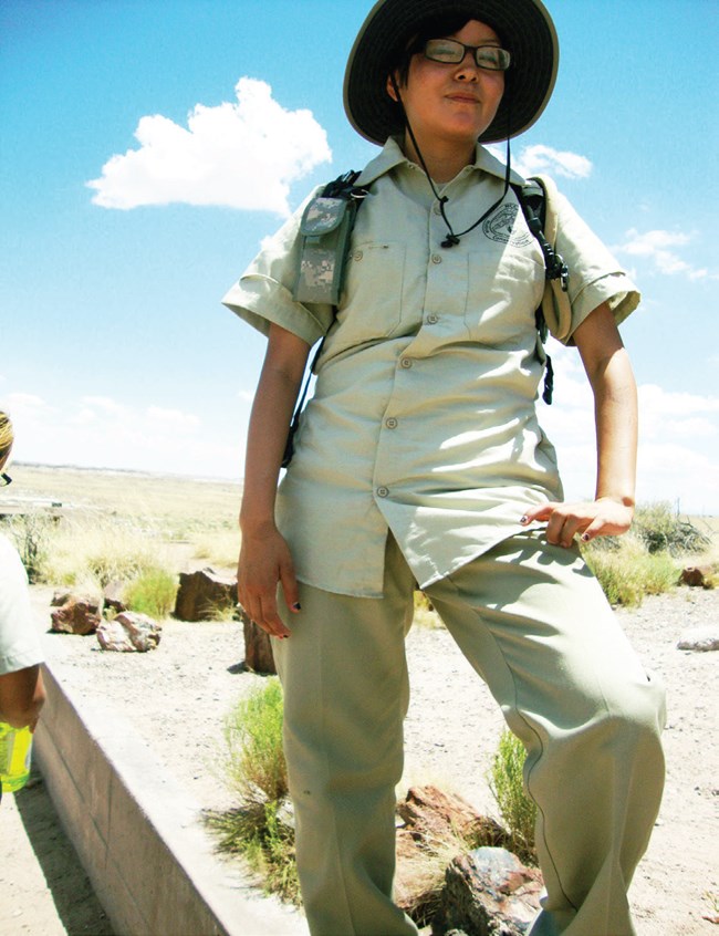 A young Native woman stands outside, dressed in khaki outdoor gear.