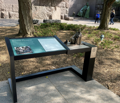 A wayside exhibit titled "Wartime President" with a graphic panel, a small replica of a nearby statue of a man with a cape, and a speaker for audio description.