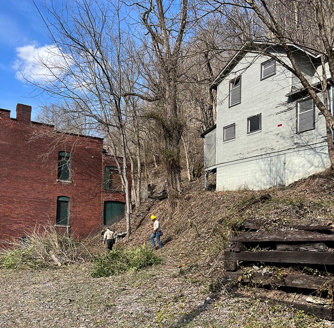 Work completed by the Veterans Fire Crew included a fuel reduction project around park historic structures. Two people near historic structures.
