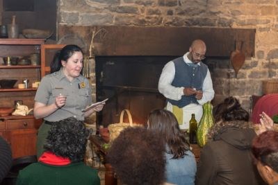 A woman in a park ranger uniform and a man in colonial period costume in front of an audience.