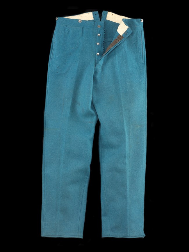 NMAH-ET2012-14993 A pair of blue trousers against a black background. The buttons are unbuttoned, and the right side is folded over