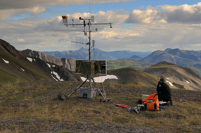 A researcher sets up a climate monitoring station in the mountains.