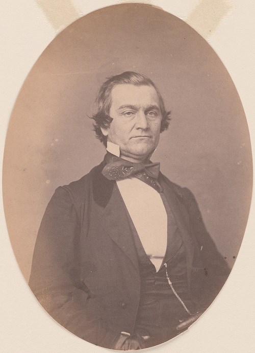 Portrait photograph of William Yancey. The photograph is sepia toned and the subject is shown from the waist up. He wears a suit and cravat, and his hairline is beginning to recede. He stares directly into the camera.