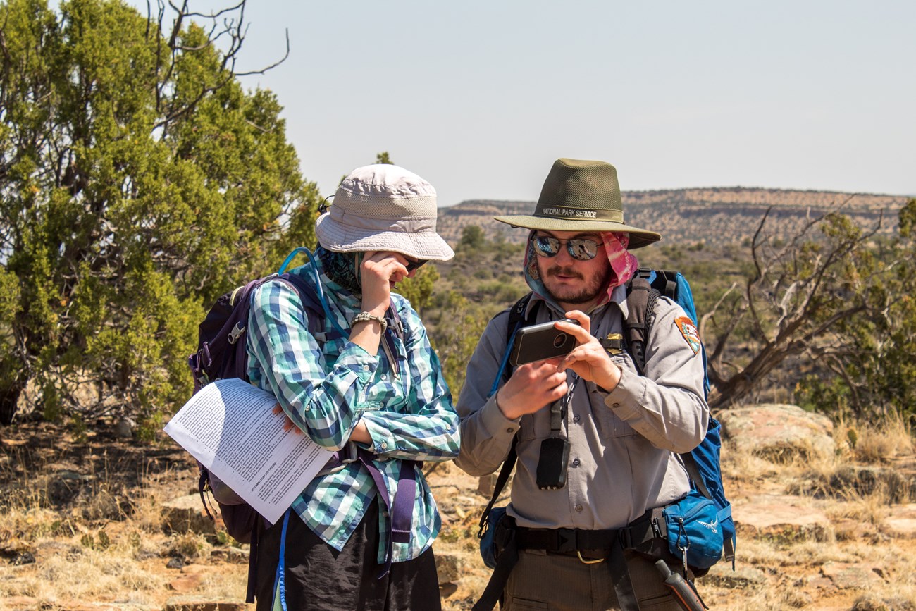 Park rangers always come prepared. Do you? Park Ranger shows hiker an image on his phone.