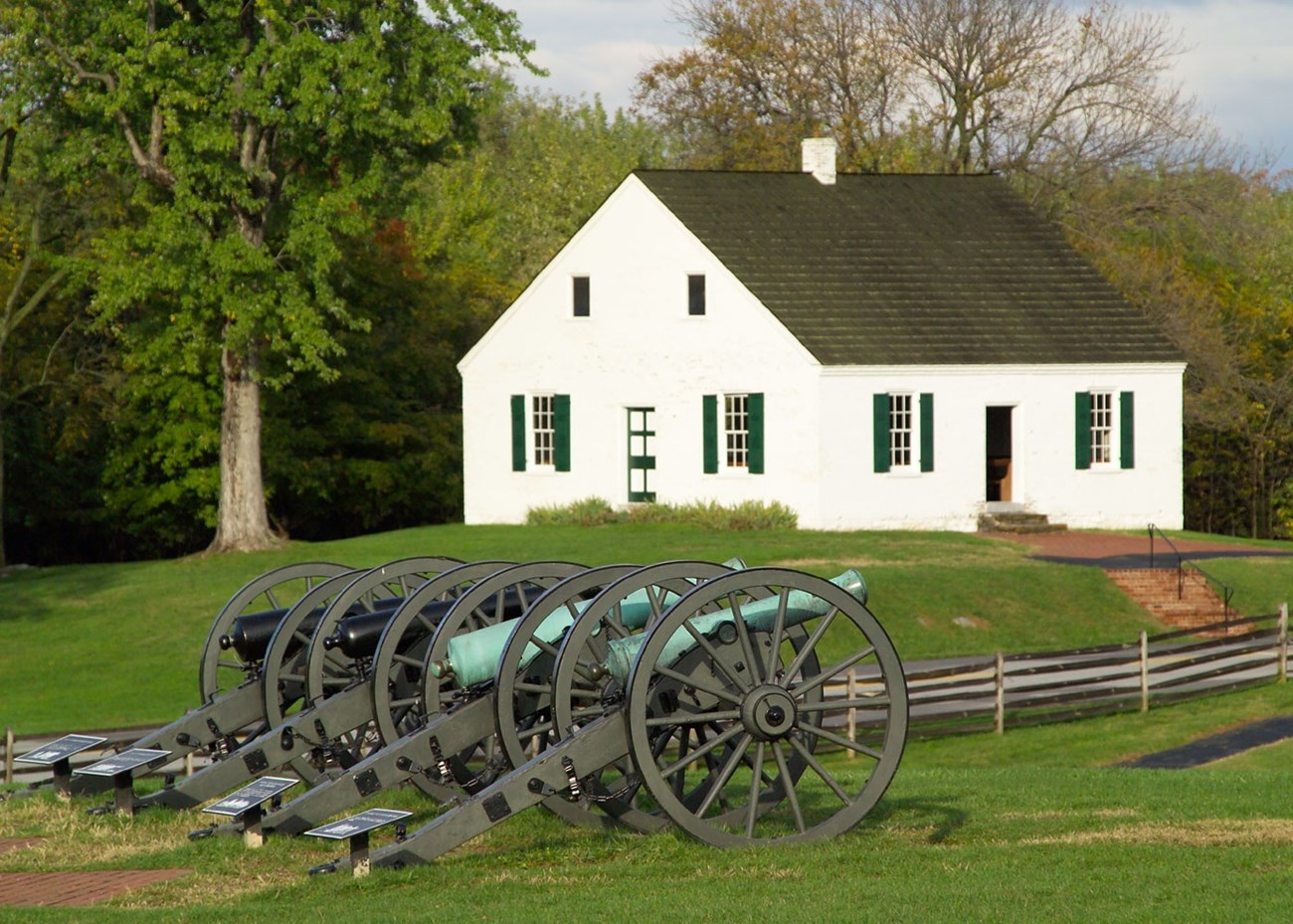 A white building in the background with four cannons in the foreground.