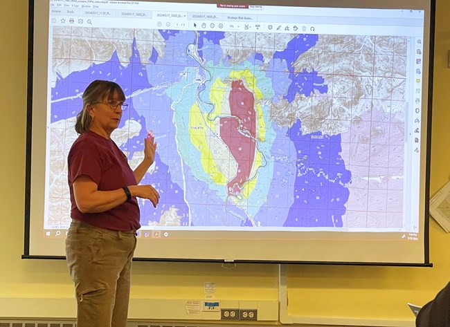 A woman stands in front of a map displayed on a screen
