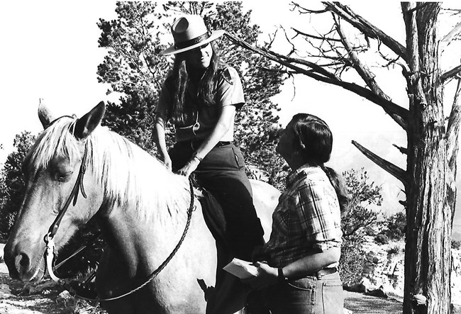 Ranger Eileen Szychowski on horseback speaking with a visitor. Eileen Szychowski on horseback talks with a visitor.