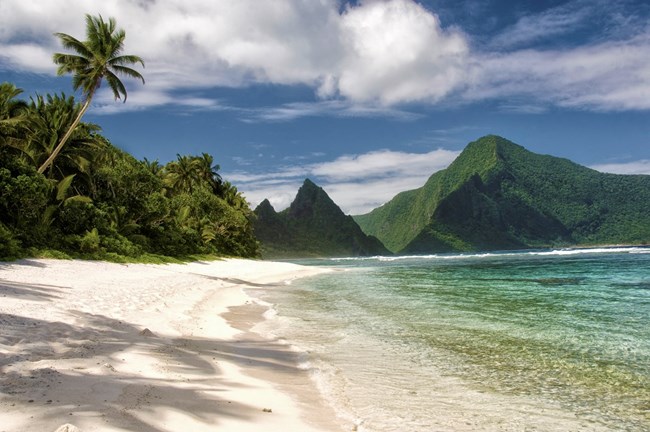a beautiful sandy beach and vegetation covered mountains of American Samoa
