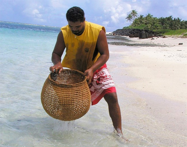 Ofu fisherman with basket fish trap Samoan man holds woven fish trap as he stands in ocean surf