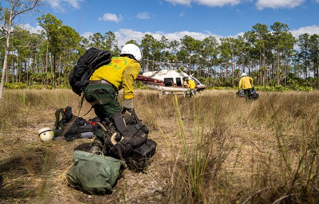 Several people carrying gear bags walk towards a helicopter