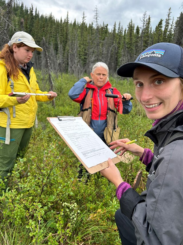 A woman holding a clipboard smiles at the camera while two other women look on