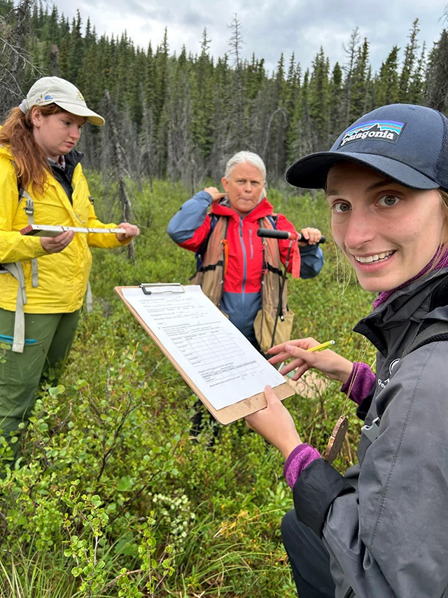 A woman holding a clipboard smiles at the camera while two other women look on