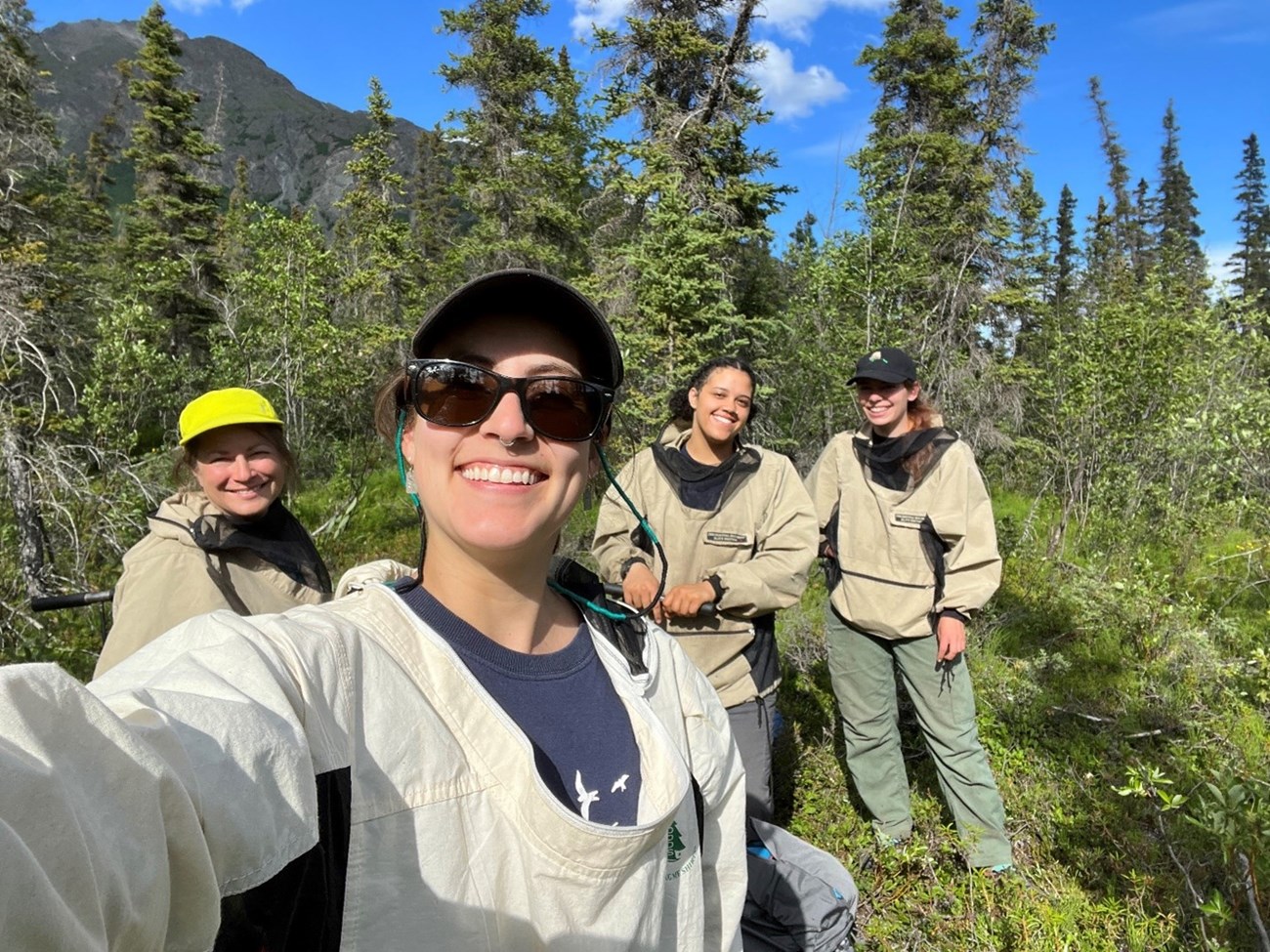 4 women smile at the camera; trees and mountains in the background