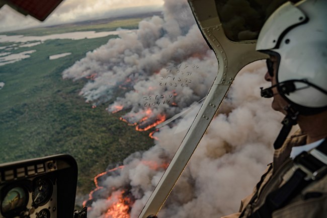 A South Florida wildland firefighter looks out a helicopter window at a wildland fire A South Florida wildland firefighter looks out a helicopter window at a wildland fire