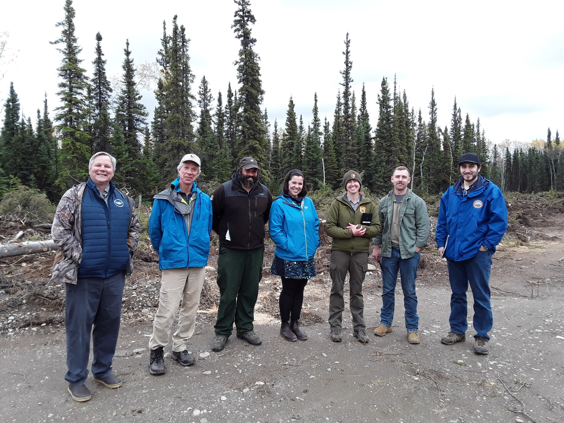 Group photo in Anderson-Clear area A group of 7 people smiles at the camera; trees in the background