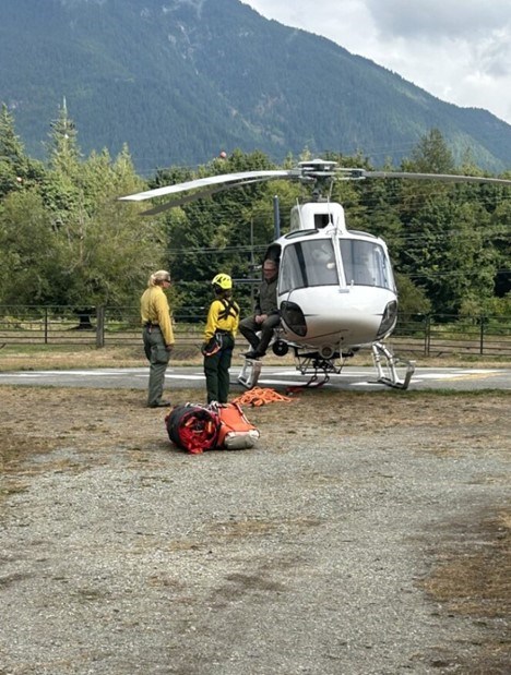 Briefing 2 people in flight suits stand near a helicopter talking to a third person in the doorway of the helicopter