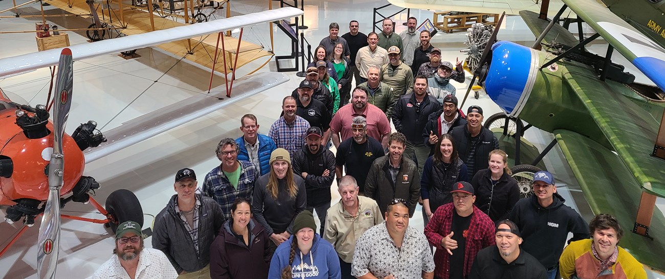 Participants pause for a photo in the Pearson Air Museum. A group of people stand amongst old aircraft in a large cavernous space.