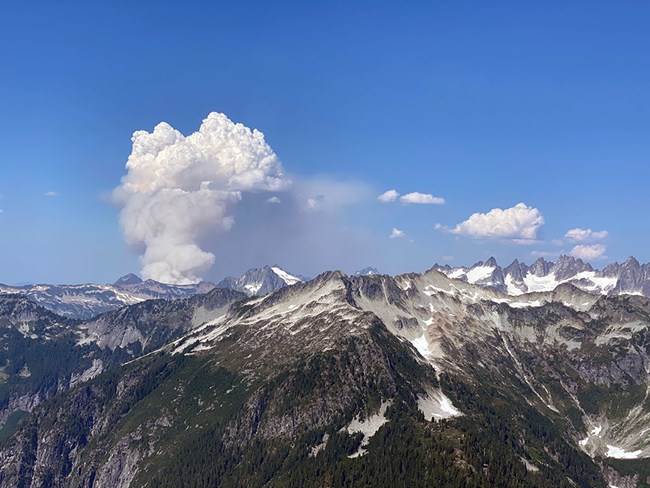Smoke plume from the Bear Creek Fire. Smoke plume rising from snowy, rocky, mountains.