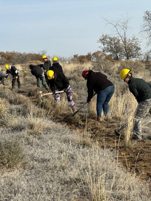 Students learn firefighting skills. People use tools to clear vegetation in a field.