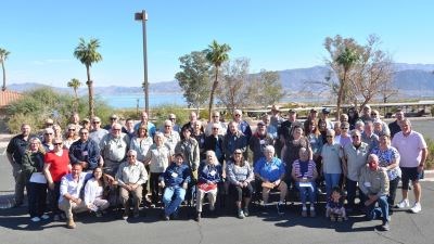 Nancy Bernard A group of volunteers stand and part staff in a parking lot with a lake and mountains in the background.