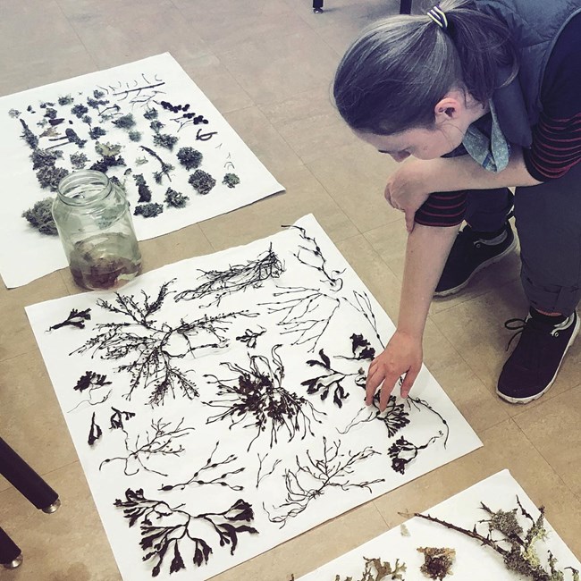 Woman crouches over artwork on floor