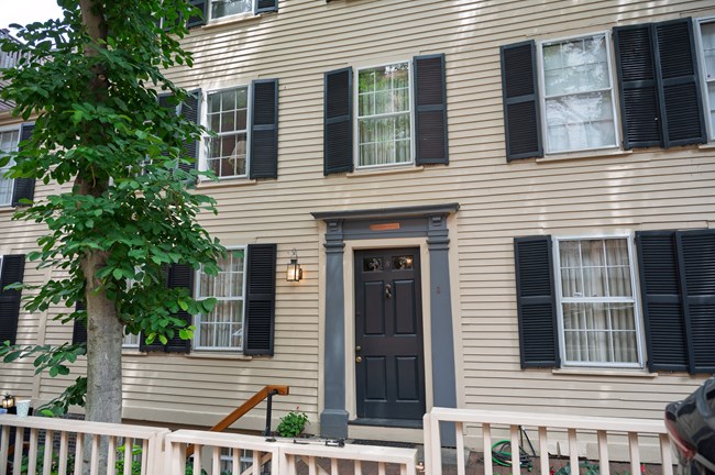 A two-story home with yellow side paneling. Two windows are on either side of the front door and three windows are across the top.