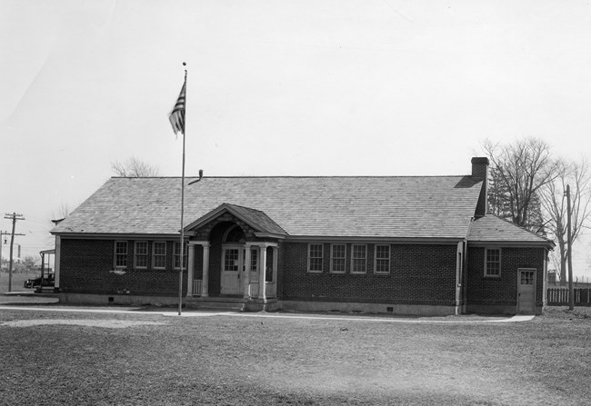 A small brick school building with a flag pole in front.