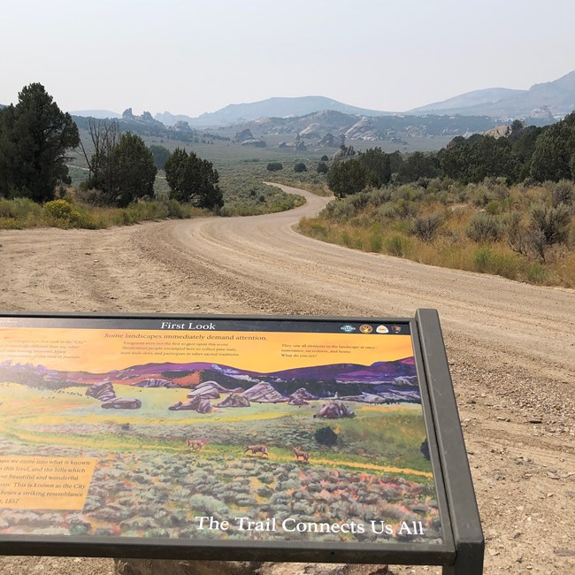 A wayside exhibit sign looking out over a dirt road and distant desert mountains.
