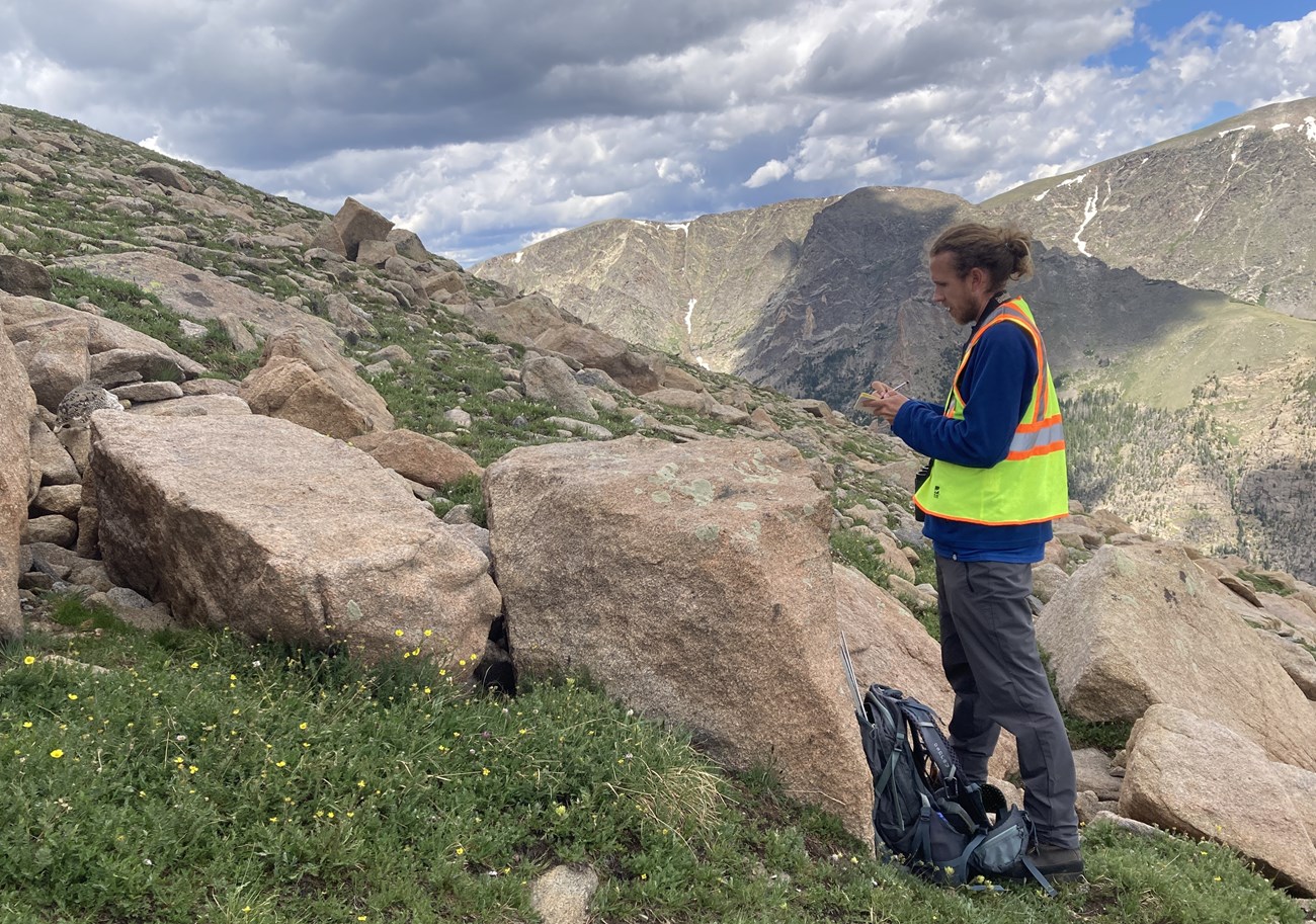 Nick Parker, Bailey Fellow, on a mountain in a rock field observing a ptarming.