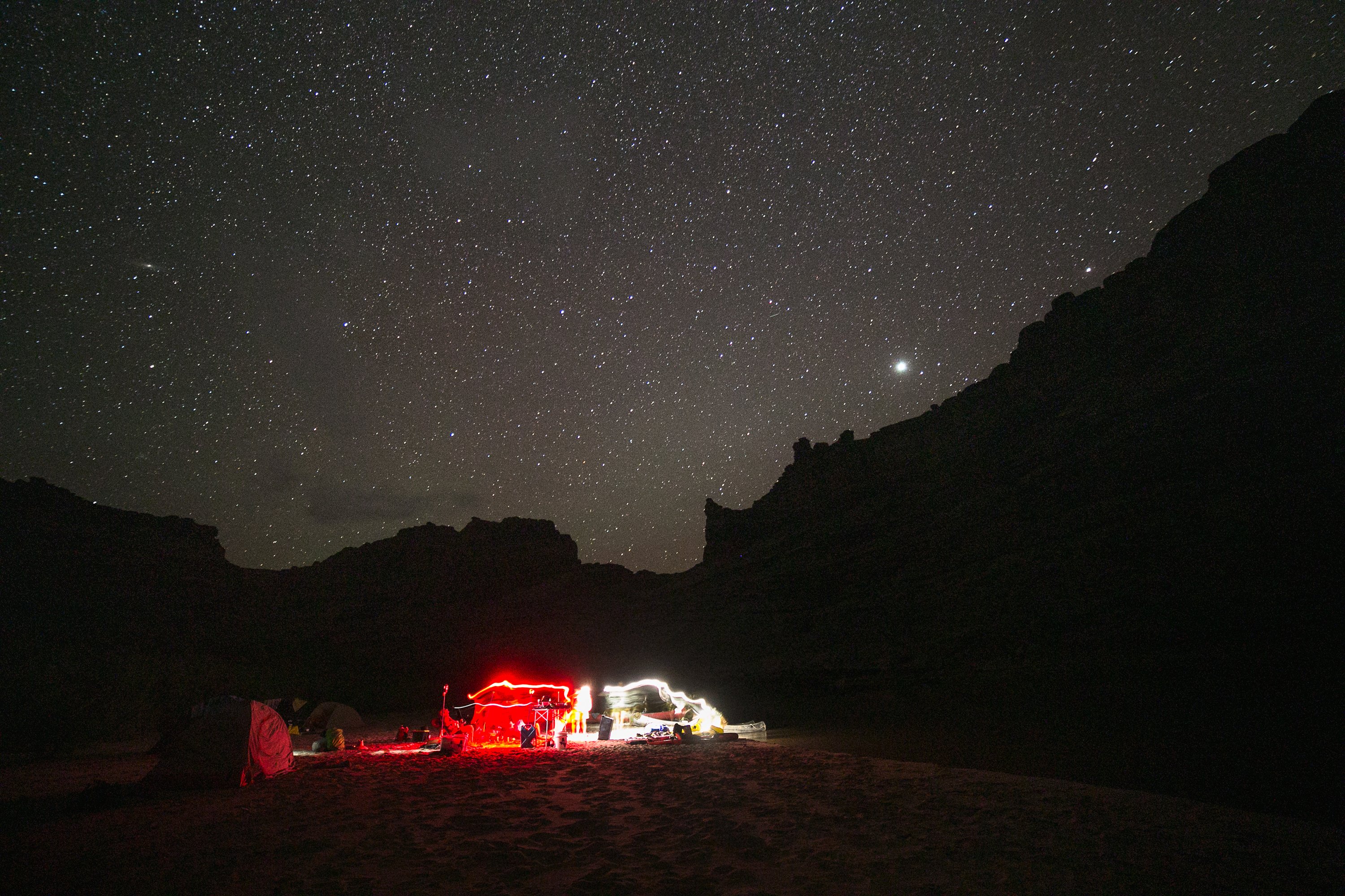 A group of campers with gear lit by red lights under a star-filled night sky