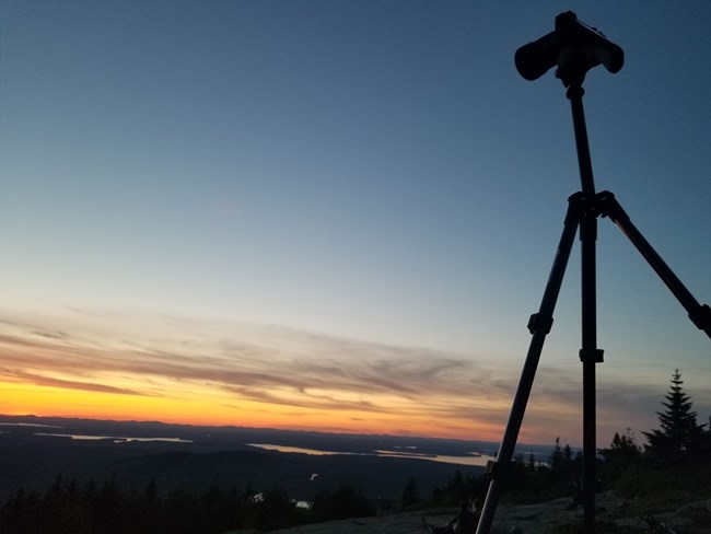 A camera on a tripod set up in front of a sunset
