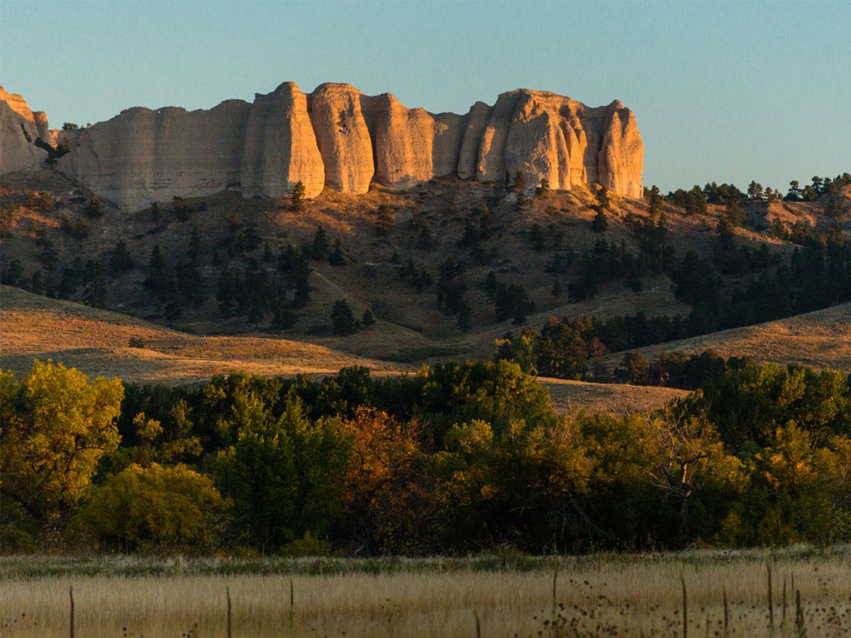 Sandstone buttes rise above grassy field, bathed in orange sunset
