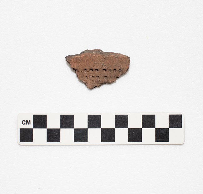 A pottery fragment with small, round indentations.