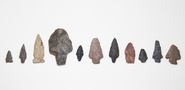 A variety of projectile points ranging in size and shape, made from many different types of raw stone material.