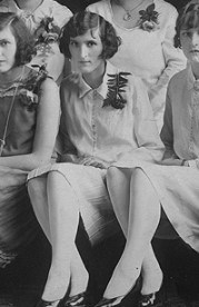 Black and white image of a young woman sitting down wearing a dress and heels.