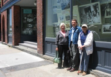 Three people stand in front of a Polish community exhibit in the windows of a brick building.